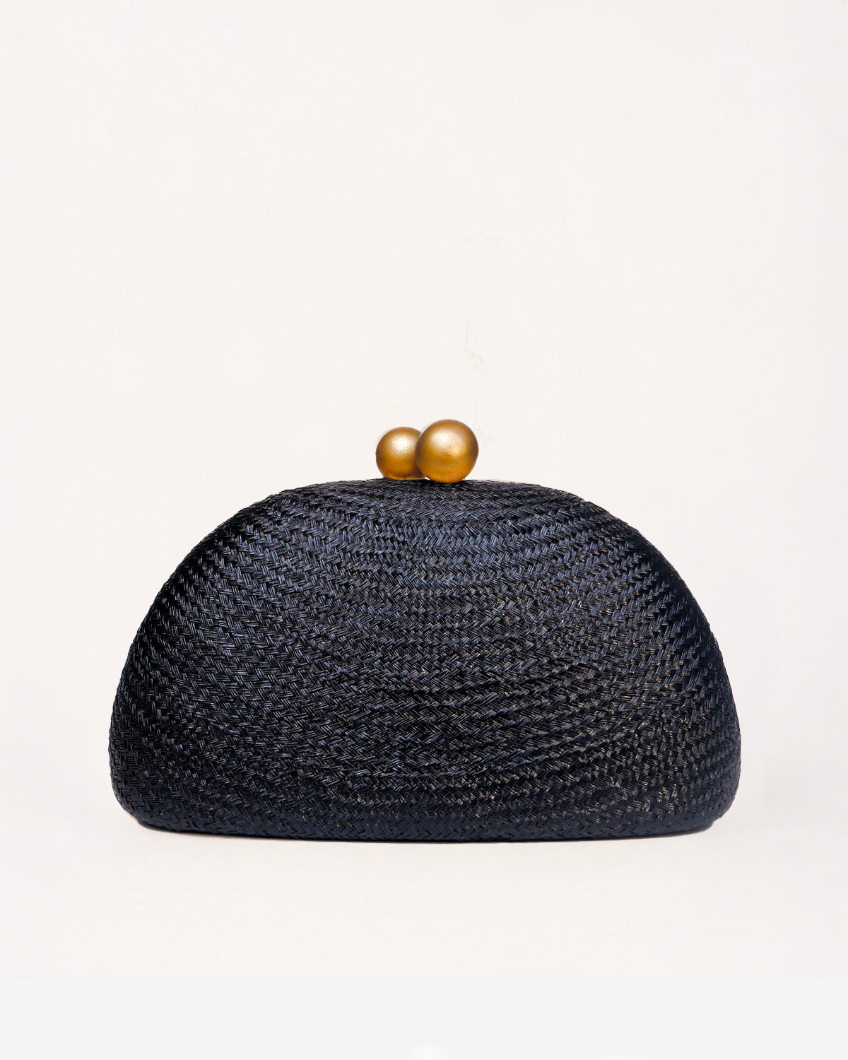 A dark black woven straw clutch bag with a dome shape and two gold wooden balls clasp, set against a plain off-white background.