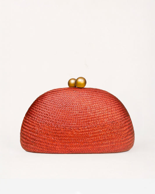 A dome-shaped woven clutch bag in a vibrant rust red-orange color, featuring a textured straw-like weave and two small metallic gold beads on top, set against a plain off-white background.