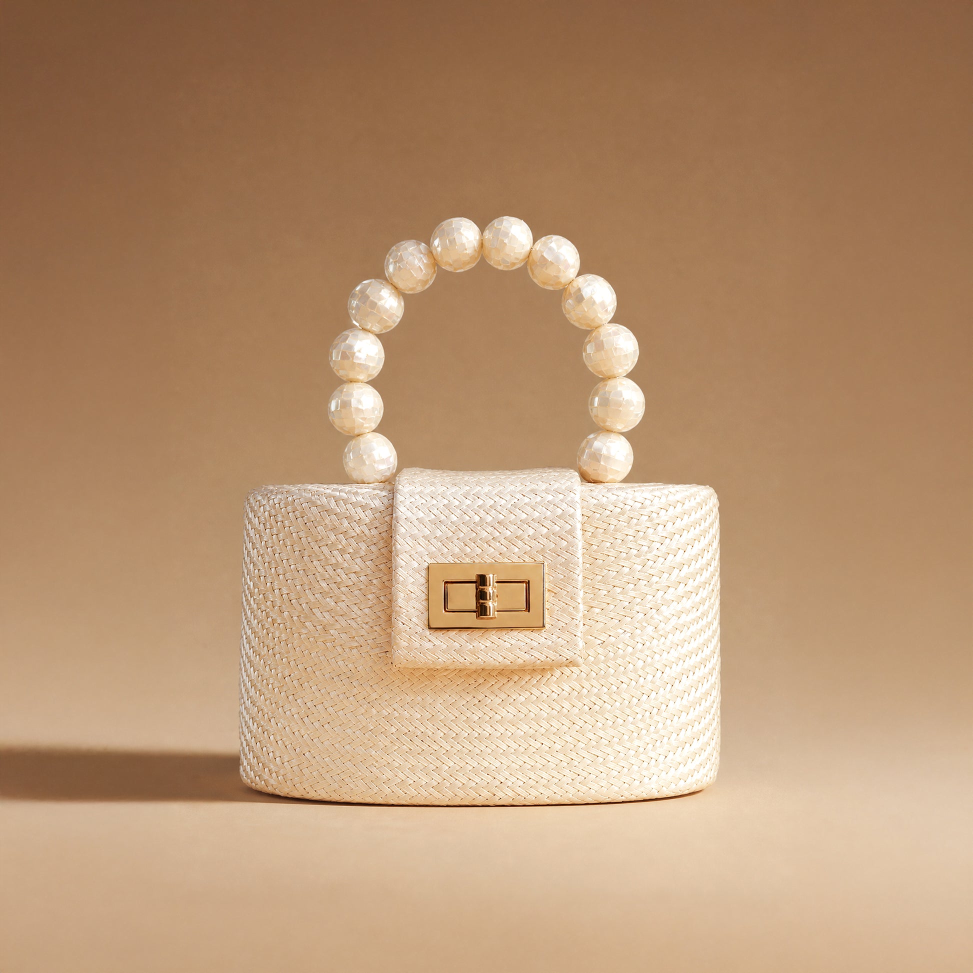 A structured cream-colored woven handbag with a beaded pearl handle and a gold-tone clasp, set against a solid warm beige background.