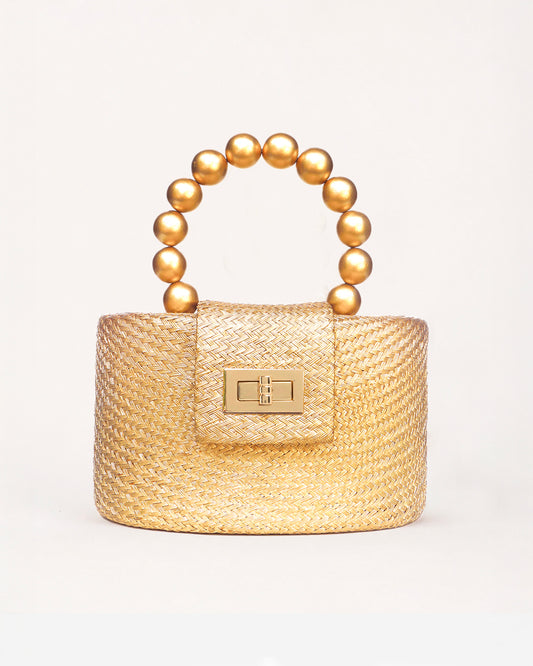 A small round structured woven handbag in warm gold-toned material with a curved top handle made of metallic gold beads and a rectangular gold-tone front clasp, shown on a clean white background.